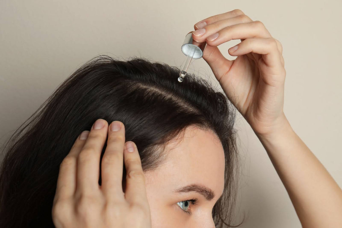 Woman applying hair serum, looking in mirror with confidence